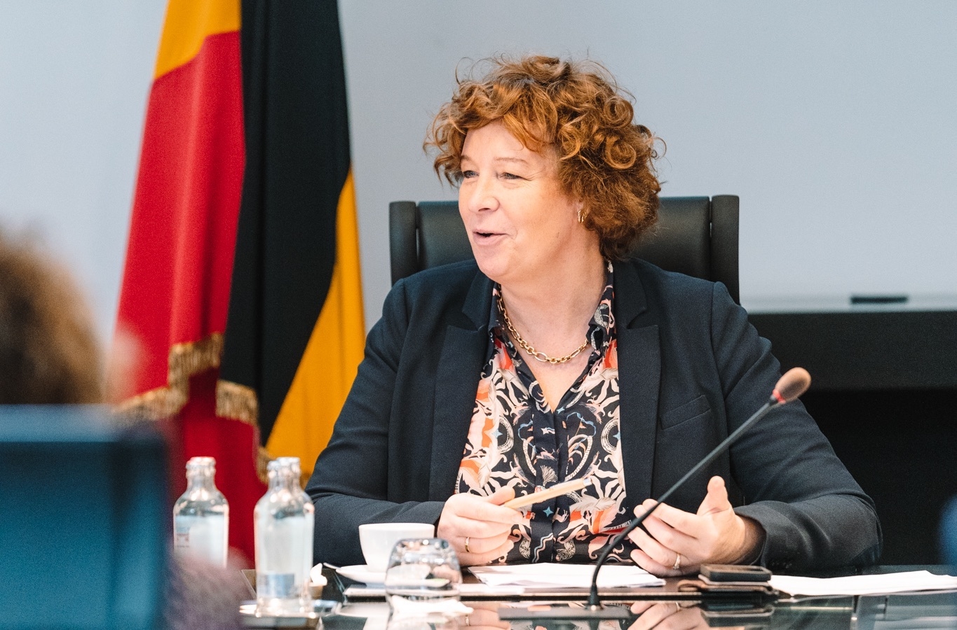 Minister Petra De Sutter tijdens een vergadering met Belgische vlag op de achtergrond